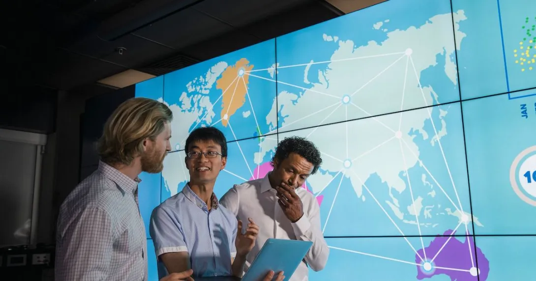 Three people standing in front of a large screen with a map of the world on it