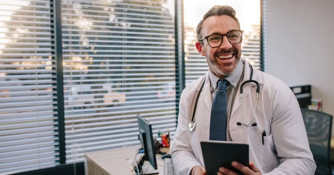 Doctor leaning against a desk while holding a tablet