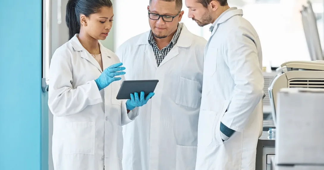 Three healthcare professionals standing in a circle looking at a tablet