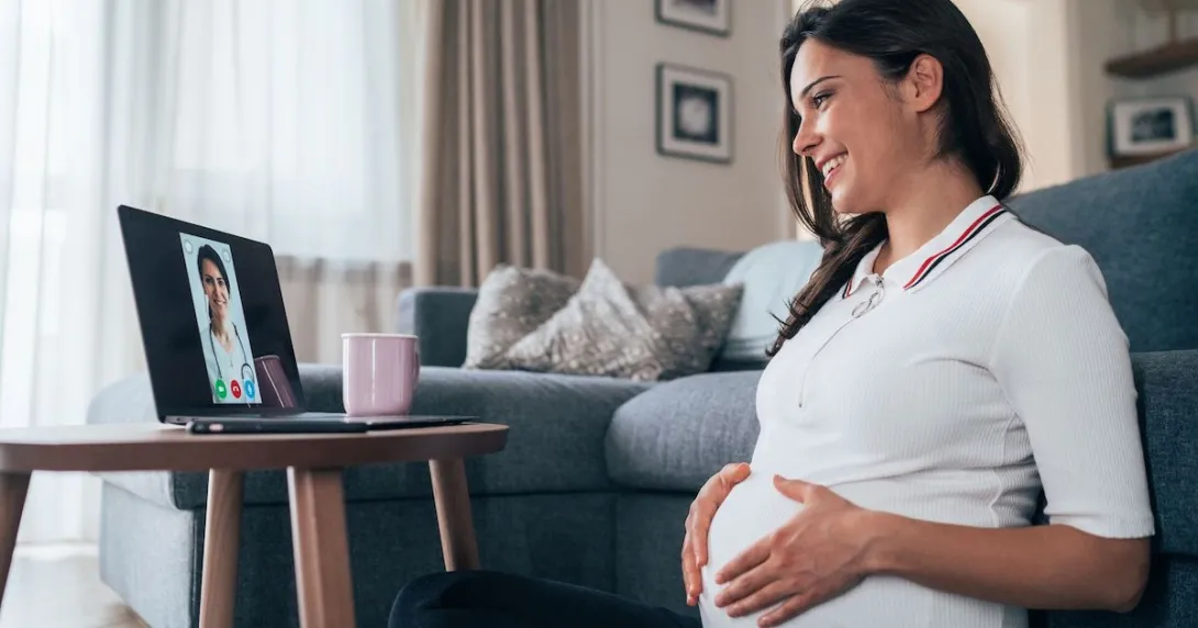 Person sitting on the floor while rubbing their pregnant belly and talking to a healthcare provider on a computer