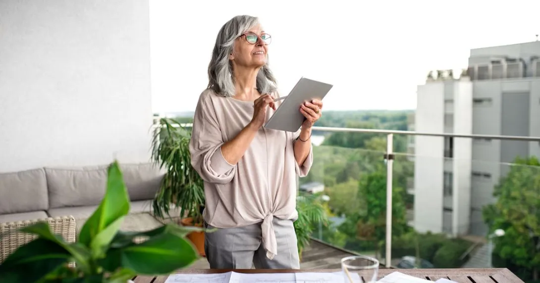 Person standing on a balcony looking at the sky with a tablet in their hand