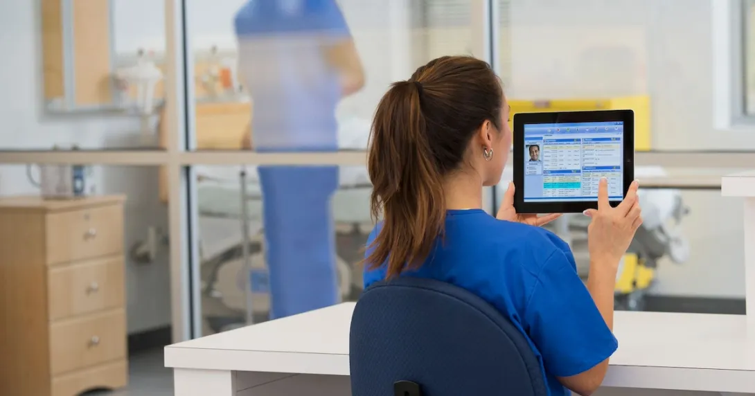 Healthcare provider in the clinical setting sitting at a desk and looking at a tablet