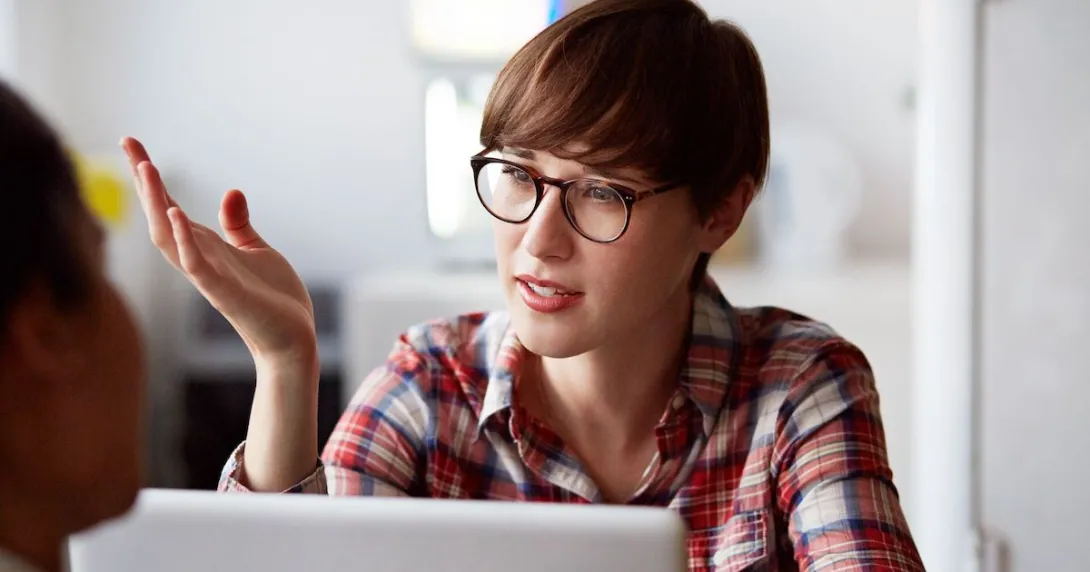 Person sitting at a computer with their hand up talking