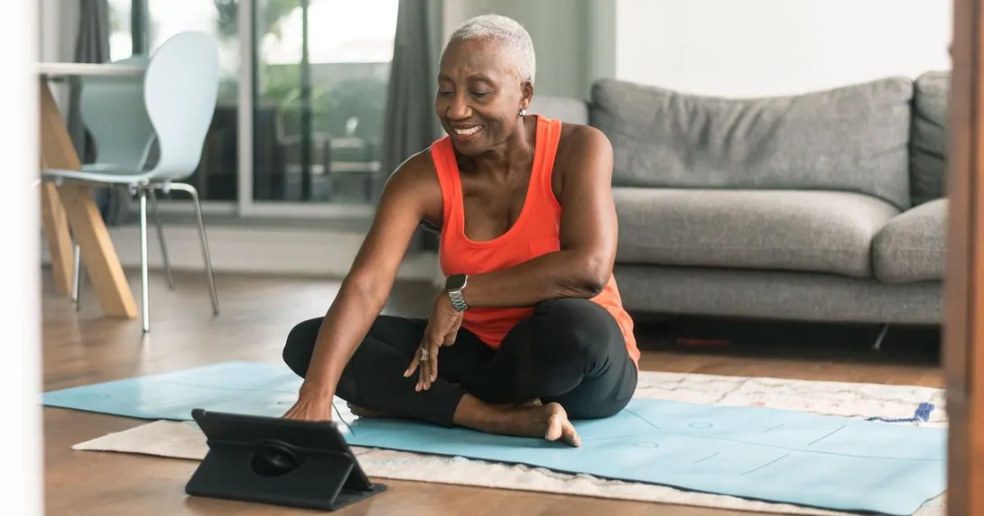 A person sitting on a yoga mat wearing workout clothes looking at tablet