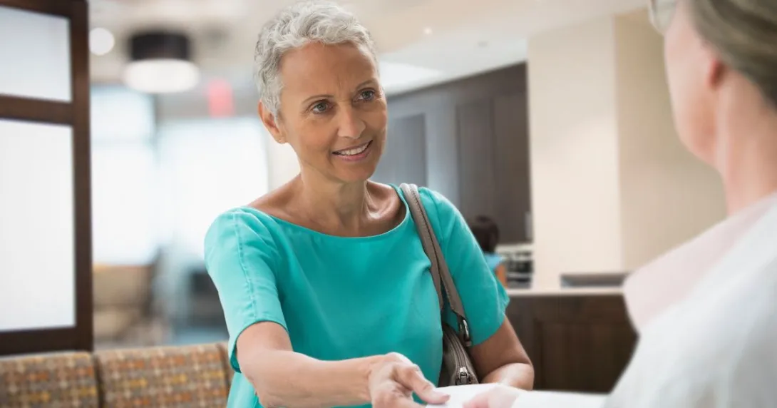 A person handing an insurance card to a front desk worker at a medical office