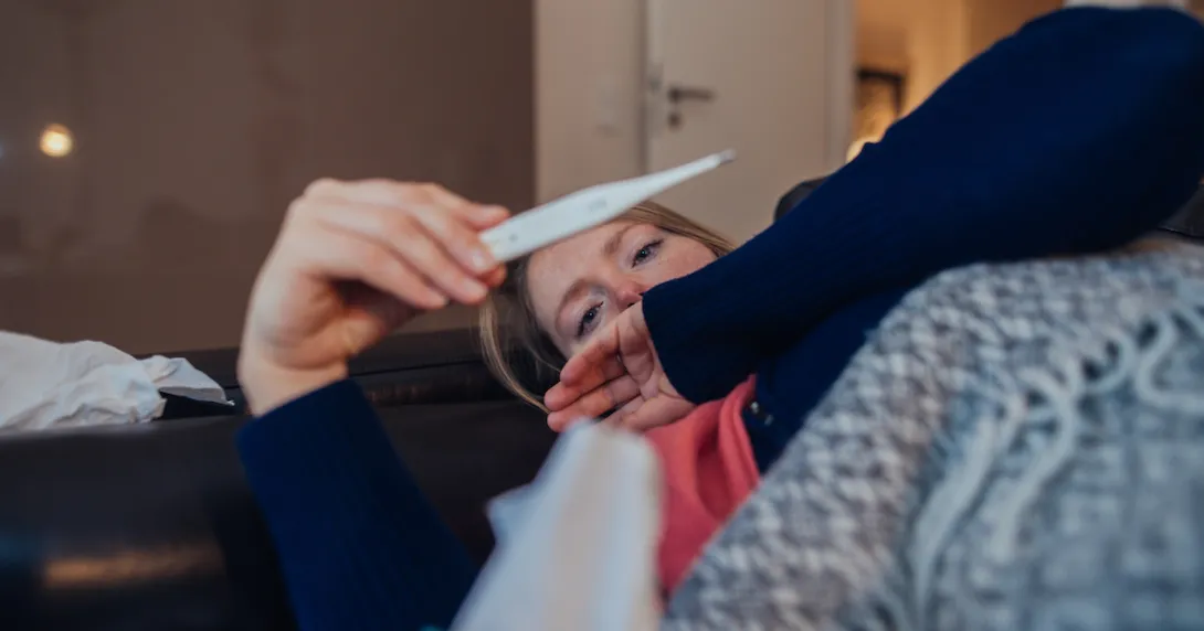 A sick woman looking a thermometer