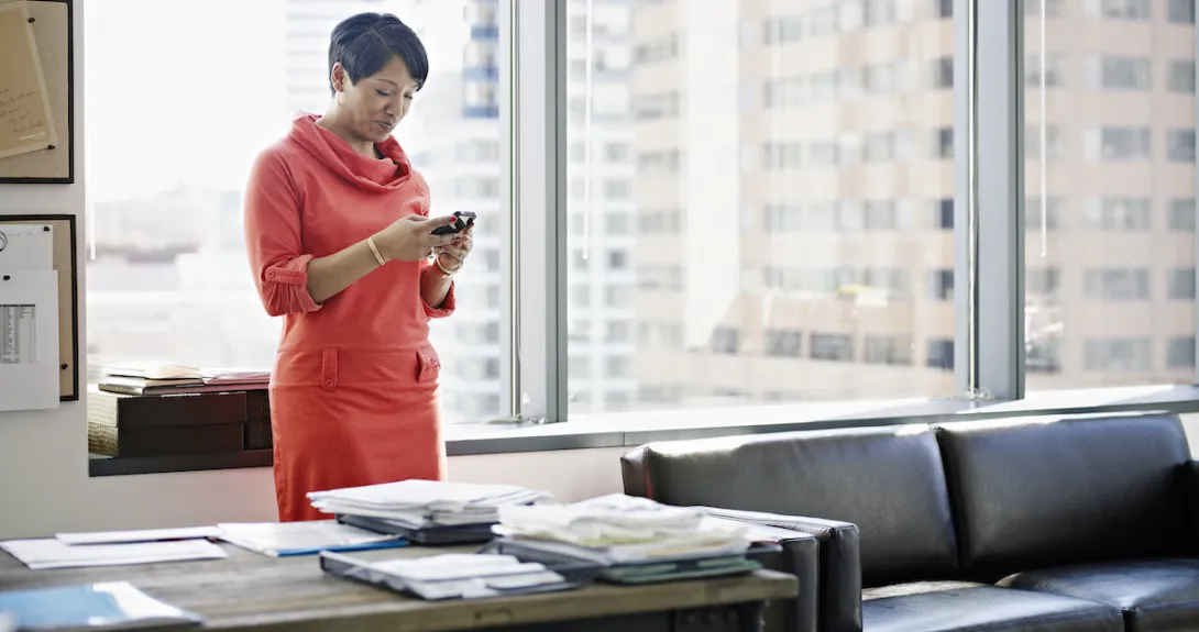 A woman standing at her desk looking down at her smartphone
